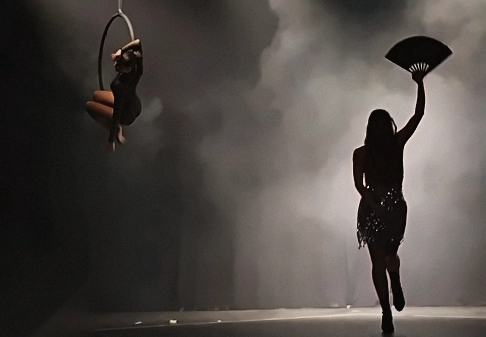 Saggio di Evolution Dance Studio: un'allieva al cerchio aereo e una danzatrice con il ventaglio, in controluce nella nebbia di scena
